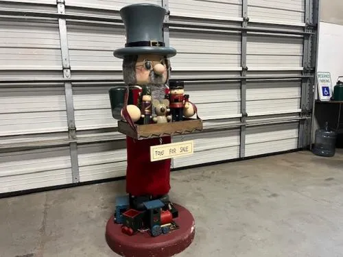 5' Old Man Nutcracker rental holding a wooden tray of toys with a "Toys for sale" sign on a wooden base